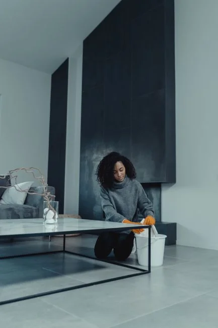 A woman cleaning the floor with a vacuum cleaner while a dog watches attentively. Indoor home setting.
